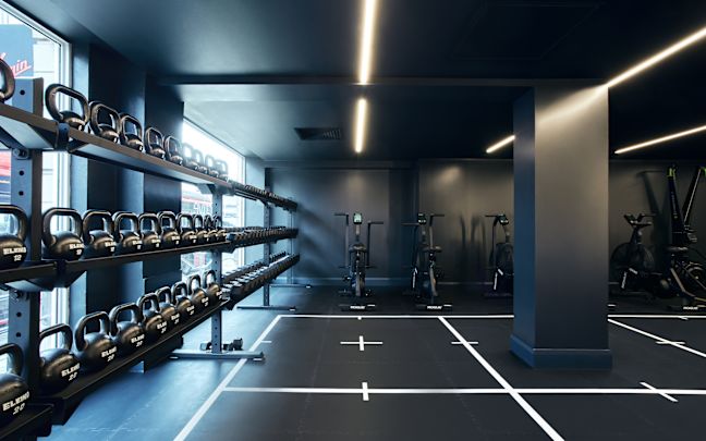 Gym floor with kettle bells on the left hand side and ergonomic bikes in the background