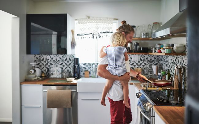 A man holding his daughter while cooking in the kitchen