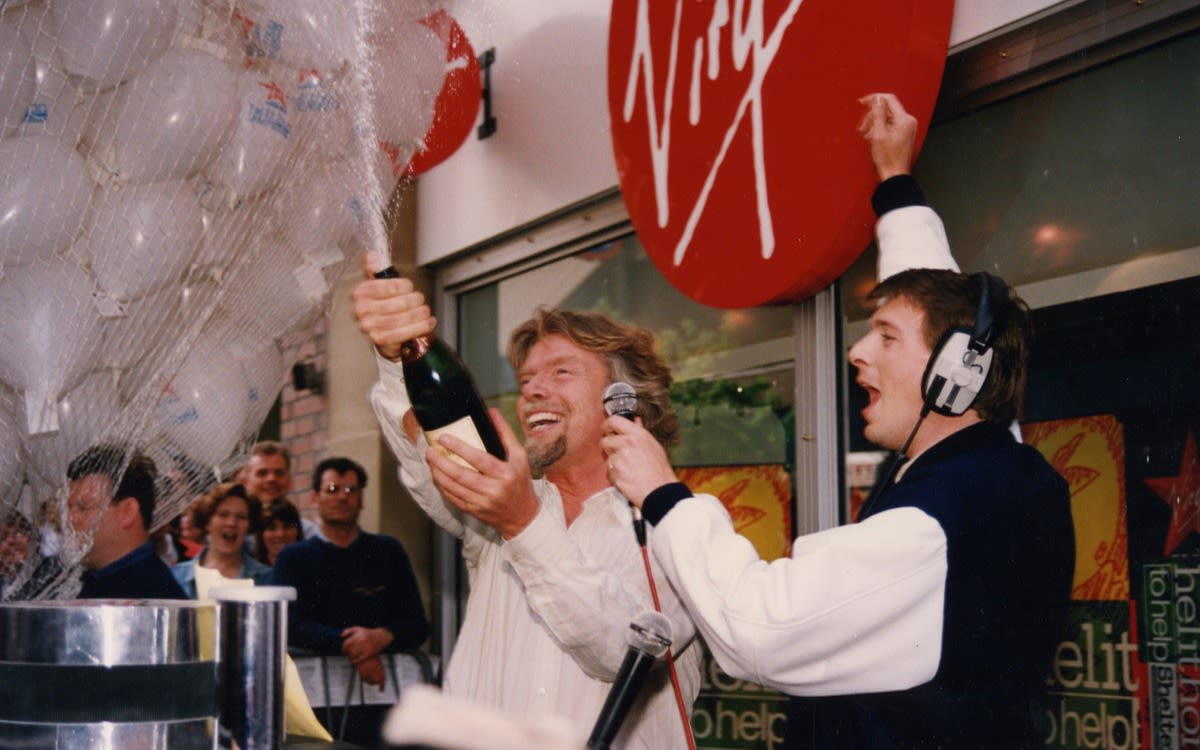 Richard Branson popping a bottle of champagne with a DJ with cheering crowds in the background