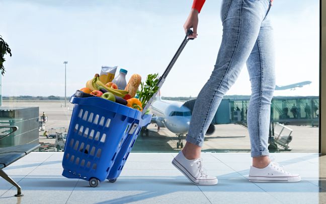 An image of a person wheeling a blue, filled Tesco shopping basket through an airport terminal. 