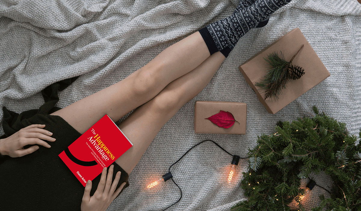 A woman rests a book in her lap while sitting on the floor with legs stretched out